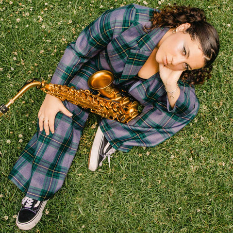 Lorren Chiodo holding an alto saxophone sitting on green grass