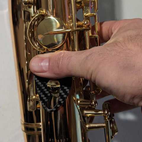 A right thumb placed on the RULON saxophone thumb rest in a natural wrist position so there is no thumb pain and the player can move and set their playing hand position naturally.