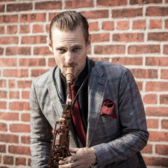 Steve Kortyka playing tenor saxophone in front of a brick wall