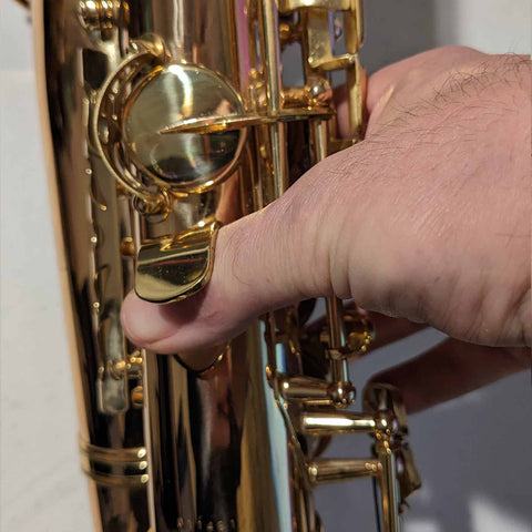 A right thumb placed into a saxophone thumb hook rest and holding the keys of the sax.
