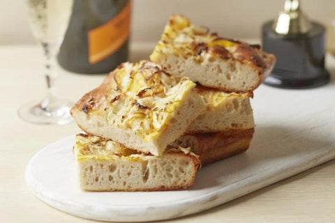 Slices of focaccia on a white plate in front of a glass of prosecco