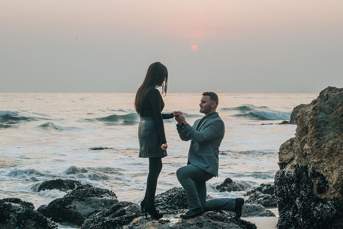 Hombre arrodillado entregando anillo a mujer a lado del mar sobre unas rocas Propuesta de matrimonio en lugares abiertos consejos monterrey carranzacarranza.com joyeria fina