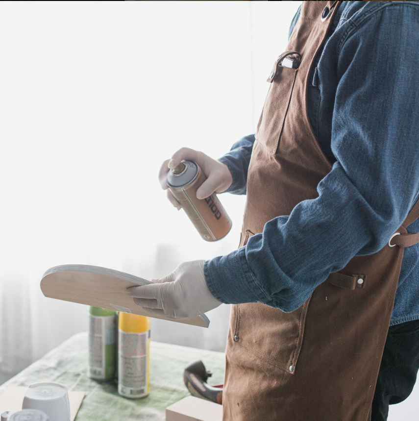 man with apron spray painting wood 