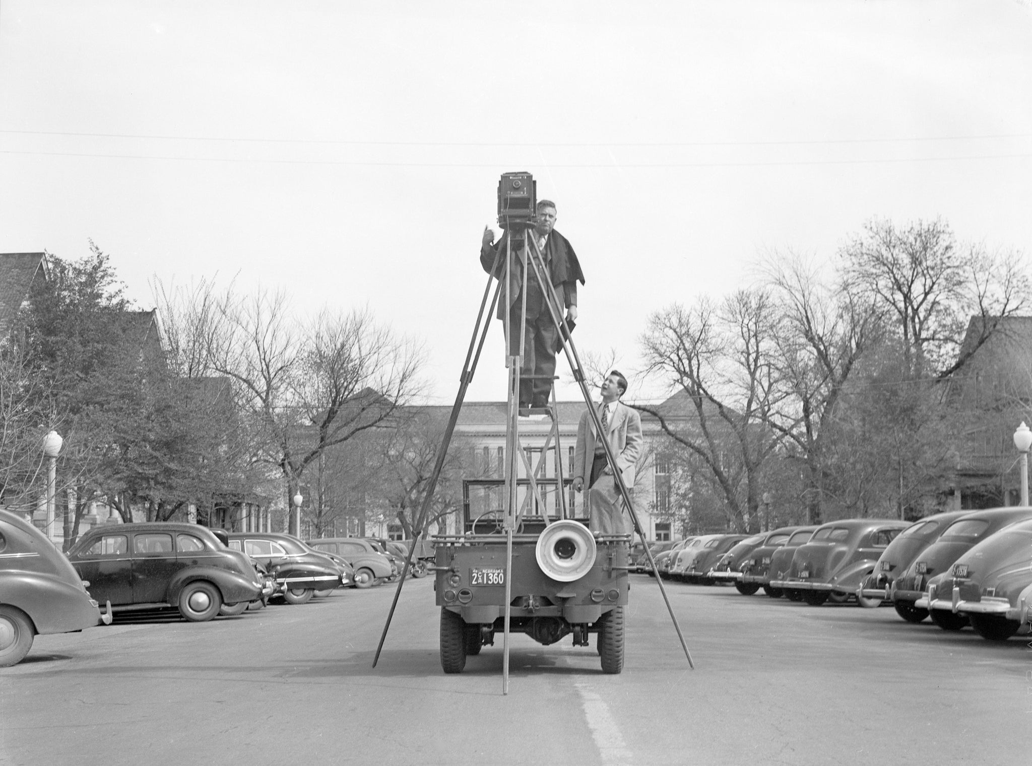 A photographer uses a large tripod to take photographs from back of a jeep on 13th & "Q" Streets, April 15, 1946. -- Nebraska State Historical Society