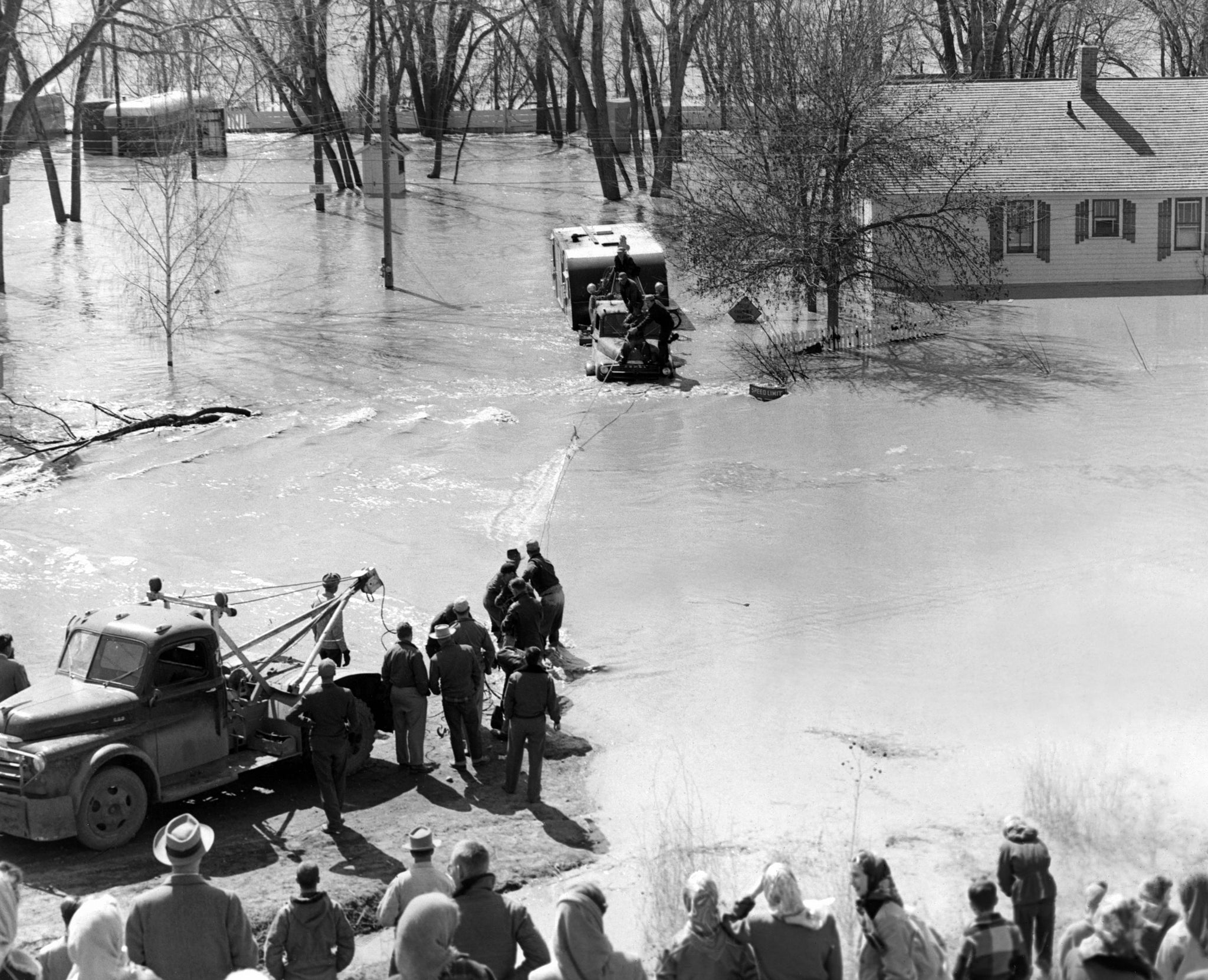 A team rescues the truck that was sent in to rescue the last trailer from Mader’s Trailer Court, Bismarck, 1952. A rescue line from the shore was thrown to the truck which stalled in the deep water while trying to pull the trailer to higher ground. Of the 52 trailers in the court, 49 were pulled out before the flood water trapped the three remaining trailers. -- BISMARCK TRIBUNE