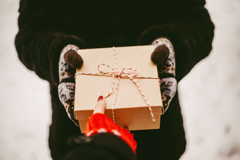 Person holding gift wrapped in brown paper with red twine