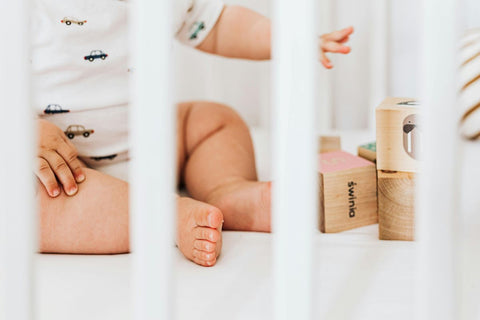 Baby's legs inside a wooden cot with wooden building blocks