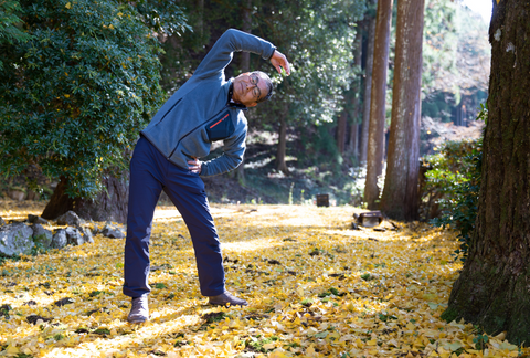 Older asian man doing a side stretch outdoors in autumn