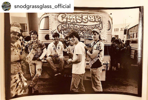 Imagen antigua de personas, asistentes a conciertos o entusiastas del vidrio, apiñados alrededor de un autobús con un cartel que dice Glass by Snodgrass.