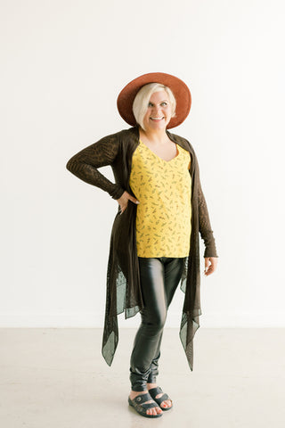 Theresa in a yellow top, flowy cardigan and black pants with a wide brim summer hat.