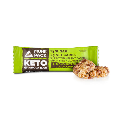 Green and black package of Munk Pack's Almond Butter Cocoa Chip Granola bar on a white background with an Almond Butter Cocoa Chip Keto Granola Bar outside of the package showing the chewy texture of nutty granola and chocolate chips. 