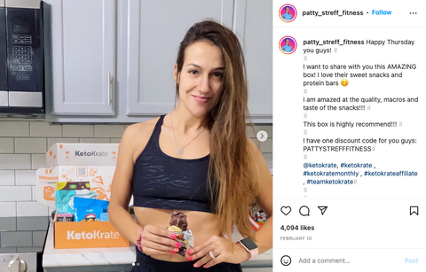 fit woman holding snack posing in front of KetoKrate holding a keto snack from her subscription box. 