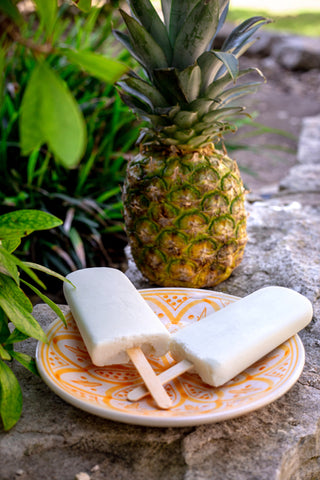 KetoKrate's keto friendly, sugar free pina colada popsicles on a plate with a pineapple and summer foliage around it