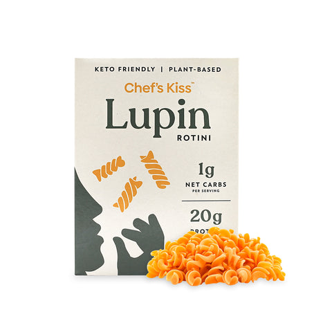 A box of Chef's Kiss Lupin Rotini pasta on a white background with a pile of 1 net carb pasta surrounding it. 