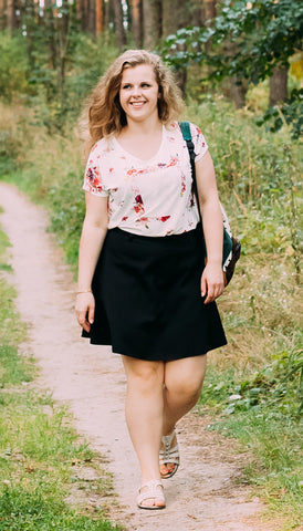 Woman walking down a path in a blush patterned top and black skirt