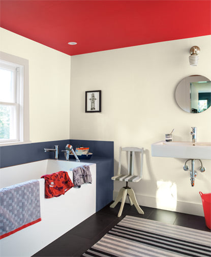 A  bathroom features a round mirror over a contemporary sink; black and white colored walls and floors are accented by a red ceiling.