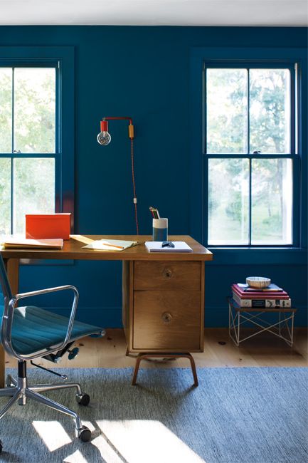 An office space features a mid-century modern wood desk complemented by varying shades of blue seen on walls, desk chair and rug.