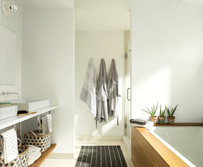 A white-painted bathroom with gray robes, wood-framed tub, boho baskets, and two sinks.