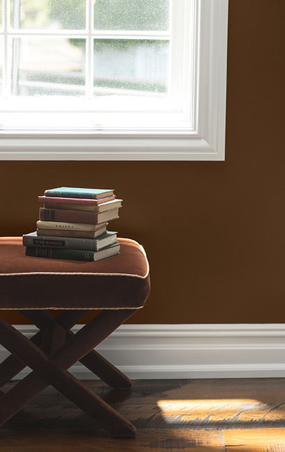 A stack of books resting on an ottoman in a brown-painted room.