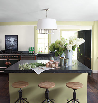 A modern green-painted kitchen with cut flowers and granite countertops.