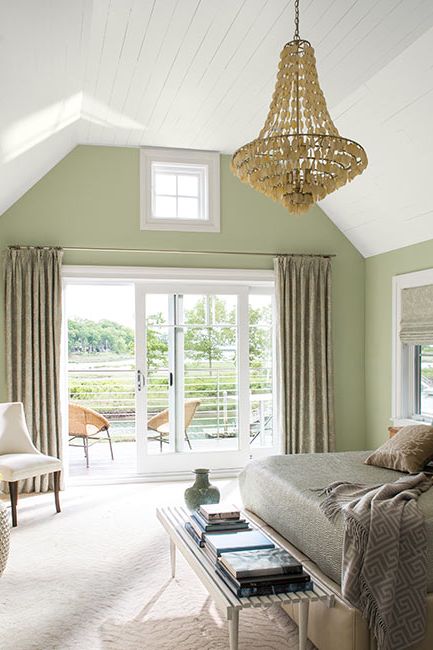 A light green-painted master bedroom with chandelier and glass sliding doors leading to outside deck.