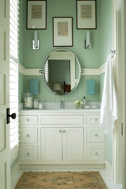 A green-painted bathroom with white built in sink cabinets and marble countertop.