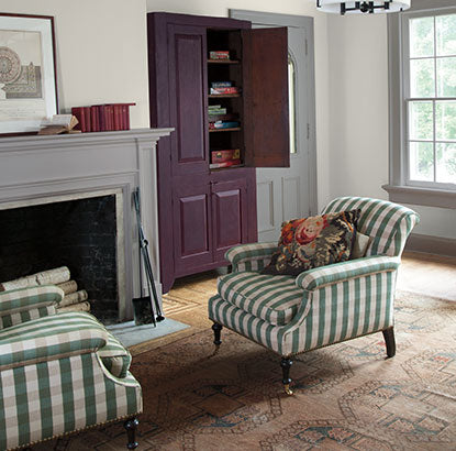 A sitting area with walls painted in Barren Plain 2111-60, fireplace, and two green striped chairs.