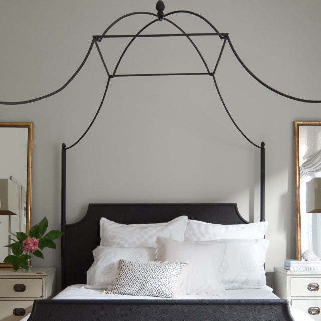 A light gray bedroom features a wrought iron four poster bed.