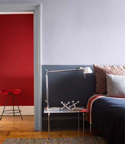 A bedroom featuring two shades of gray is beautifully contrasted by a red hallway beyond its open door.
