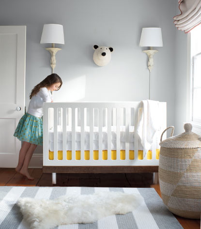 A pale blue gray nursery features a white crib overseen by a big sister.