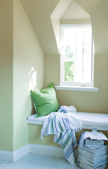 Underneath a recessed window set within a vaulted ceiling, a cozy alcove offers an inviting seating area complete with striped blanket and a large stack of magazines.