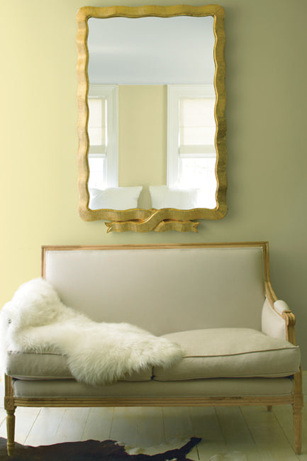 A delicate, cream-colored settee accented with a white fur throw beckons underneath an oversized, gold-framed mirror with a black and white cowhide rug on the floor.