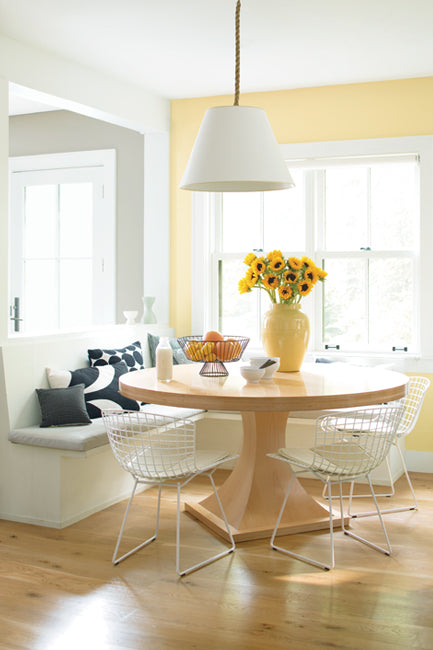 Natural light streams into a welcoming breakfast nook including a built-in bench, a round kitchen table and contemporary chairs underneath a pendant chandelier.