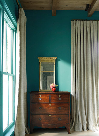 Green-painted bedroom with wooden dresser, gold mirror, and floor-length curtains.