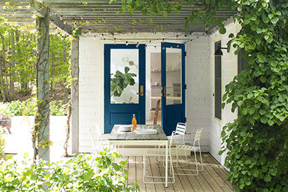 A back porch covered in ivy with blue-painted doors, white walls, and chair and table.