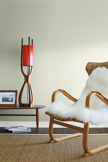 A midcentury modern wood chair with a fur covering next to a wood table and lamp in a light gray room. 