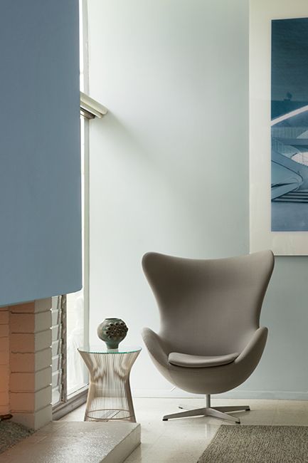 A modern gray chair and metal side table in a room with white walls that have a blue undertone.