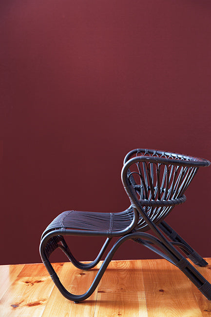 Deep red walls with a black midcentury modern chair.