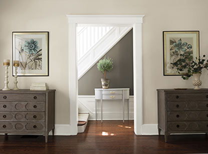 A gray hallway with white staircase and wainscoting includes a delicate console table and lustrous hardwood floors.