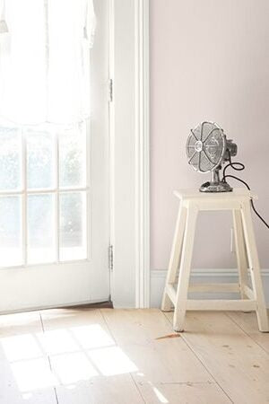 A fan sits on a white stool, and a white button up is hanging on a door.