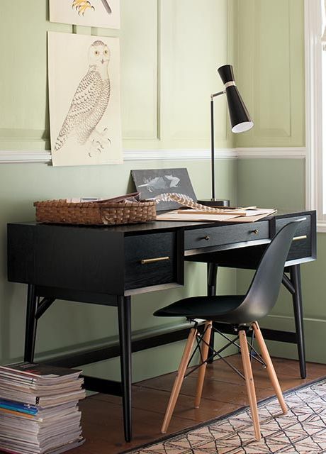 A monochromatic home office featuring two-toned green walls with two photos hanging above a black desk and chair.