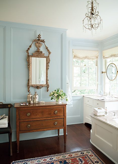 Soft blue bathroom walls with a mirror hung above a wood dresser.