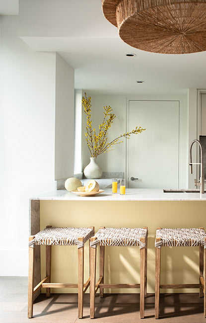 Small kitchen with white-painted walls, a yellow kitchen island and three rattan barstools.
