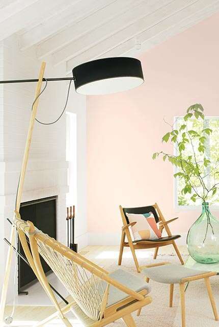 Vibrant living room with white beam ceilings and a light pink-painted accent wall featuring three chairs and a sofa.