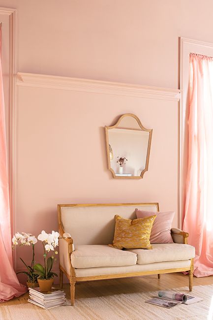 Coral pink-painted walls and matching trim with a hanging mirror above an off-white love seat.