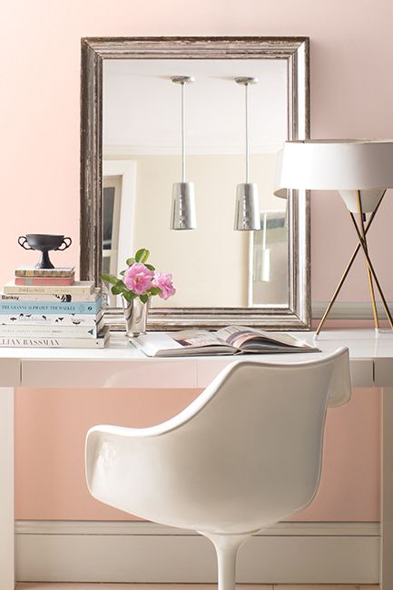 Two-toned pink-painted walls with a leaning mirror above a white desk and chair.