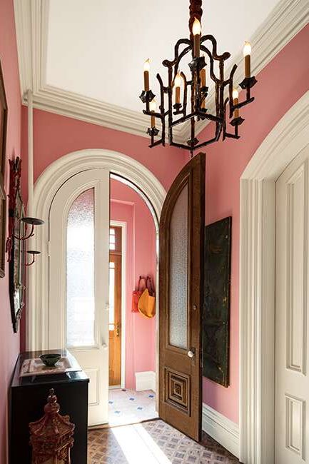 An entryway painted in Delicate Rose, with Niveous trim, a collection of wall art, large doors, and ornate chandelier.