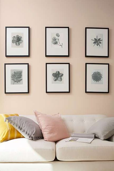 Dusty pink-painted walls with six picture frames hung above a white couch with yellow, pink, and gray throw pillows.