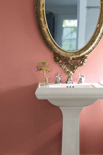Rose-painted bathroom walls with a gold mirror above a white sink.