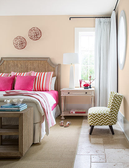 Peach-painted bedroom walls with a green chevron chair, side table, and bed featuring pink bedding.